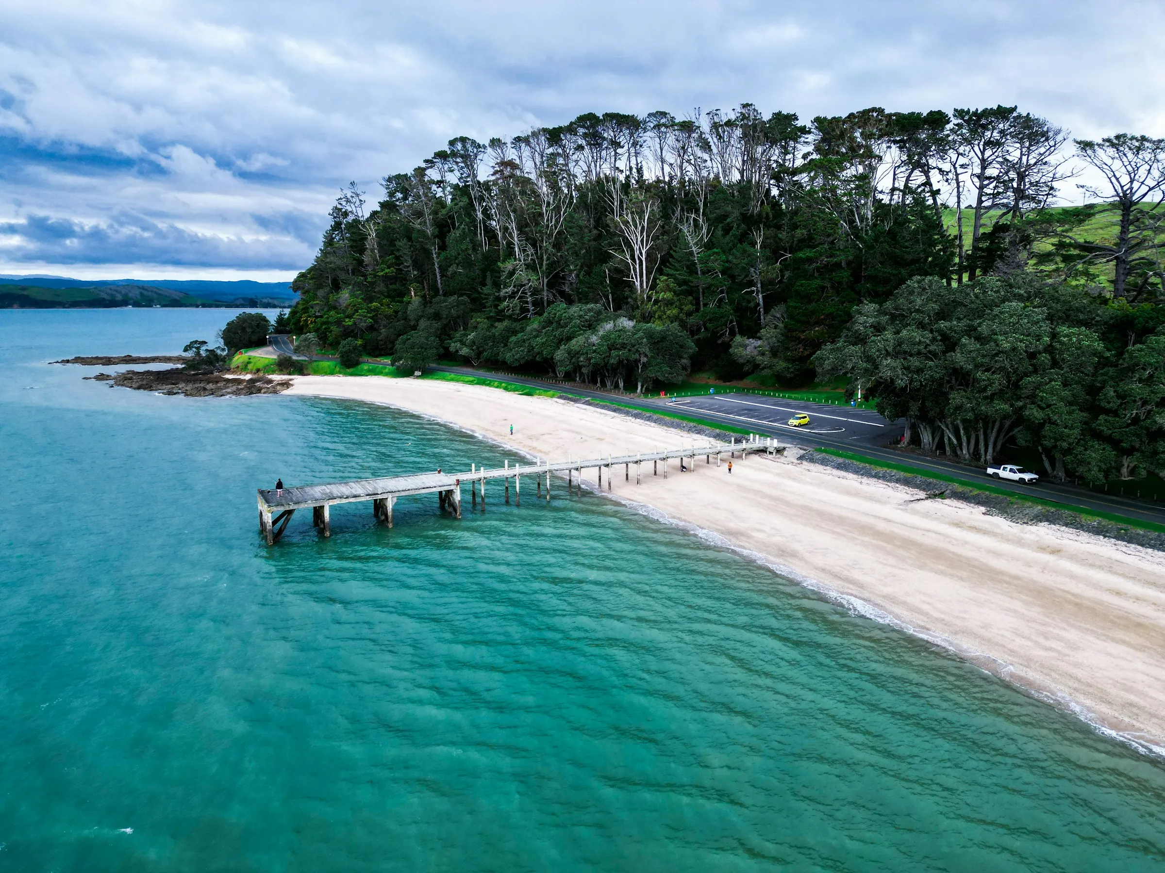 A white-sand beach and jetty with turquoise water near Auckland on a sunny day