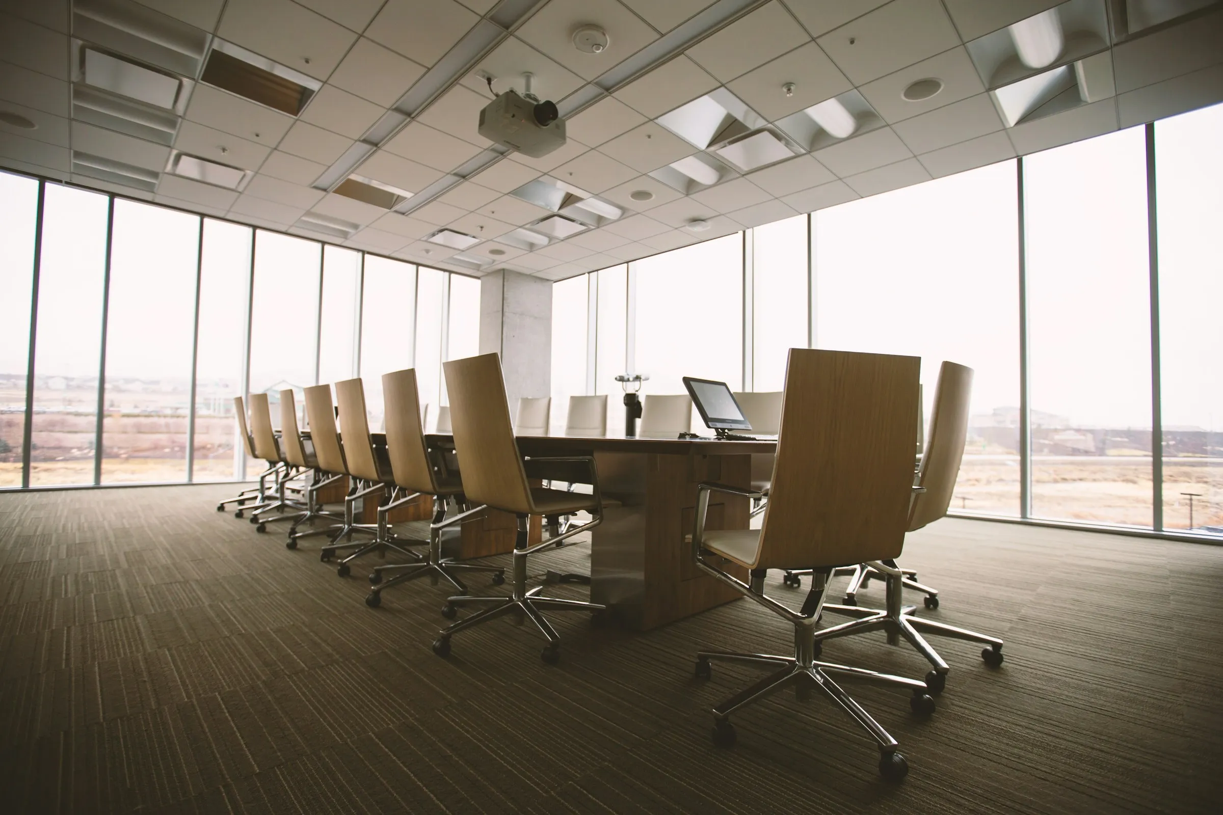 An empty, light-filled boardroom with a long timber table, rows of chairs and floor-to-ceiling windows