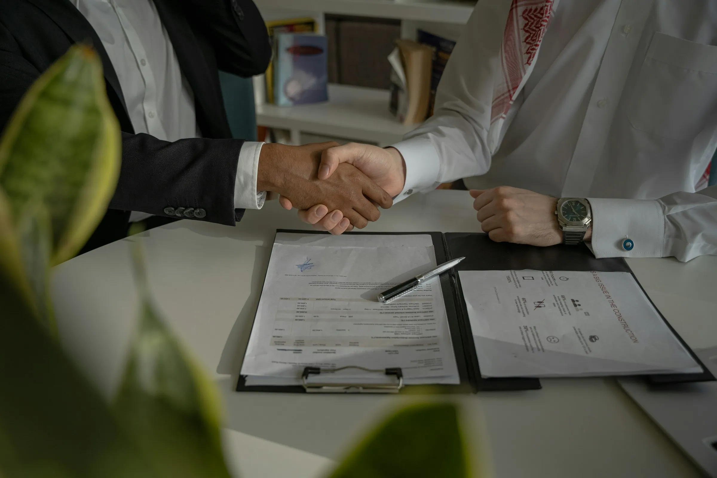 Two people shaking hands across a desk over signed loan documents and a pen